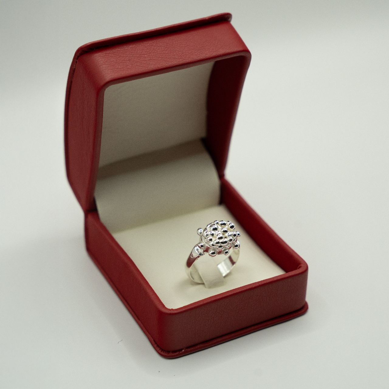 Silver ring in a red jewelry box on a light gray background