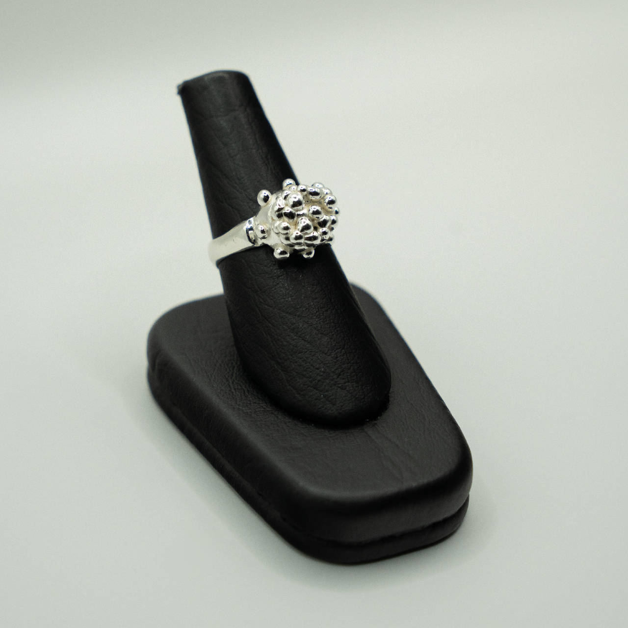 Silver ring on a black stand against a light gray background